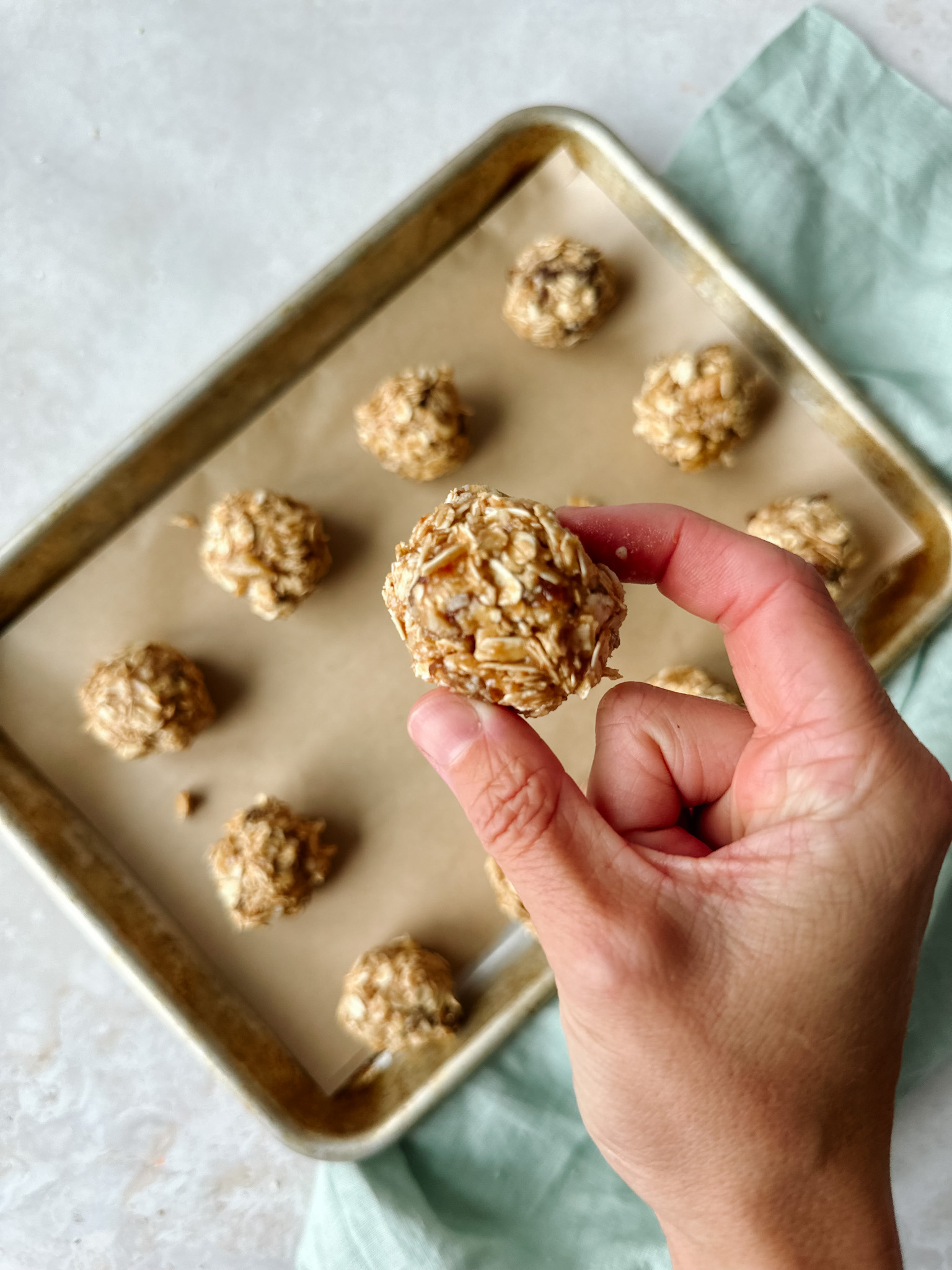 Oatmeal Raisin Energy Balls on a baking sheet with a hand holding one energy ball