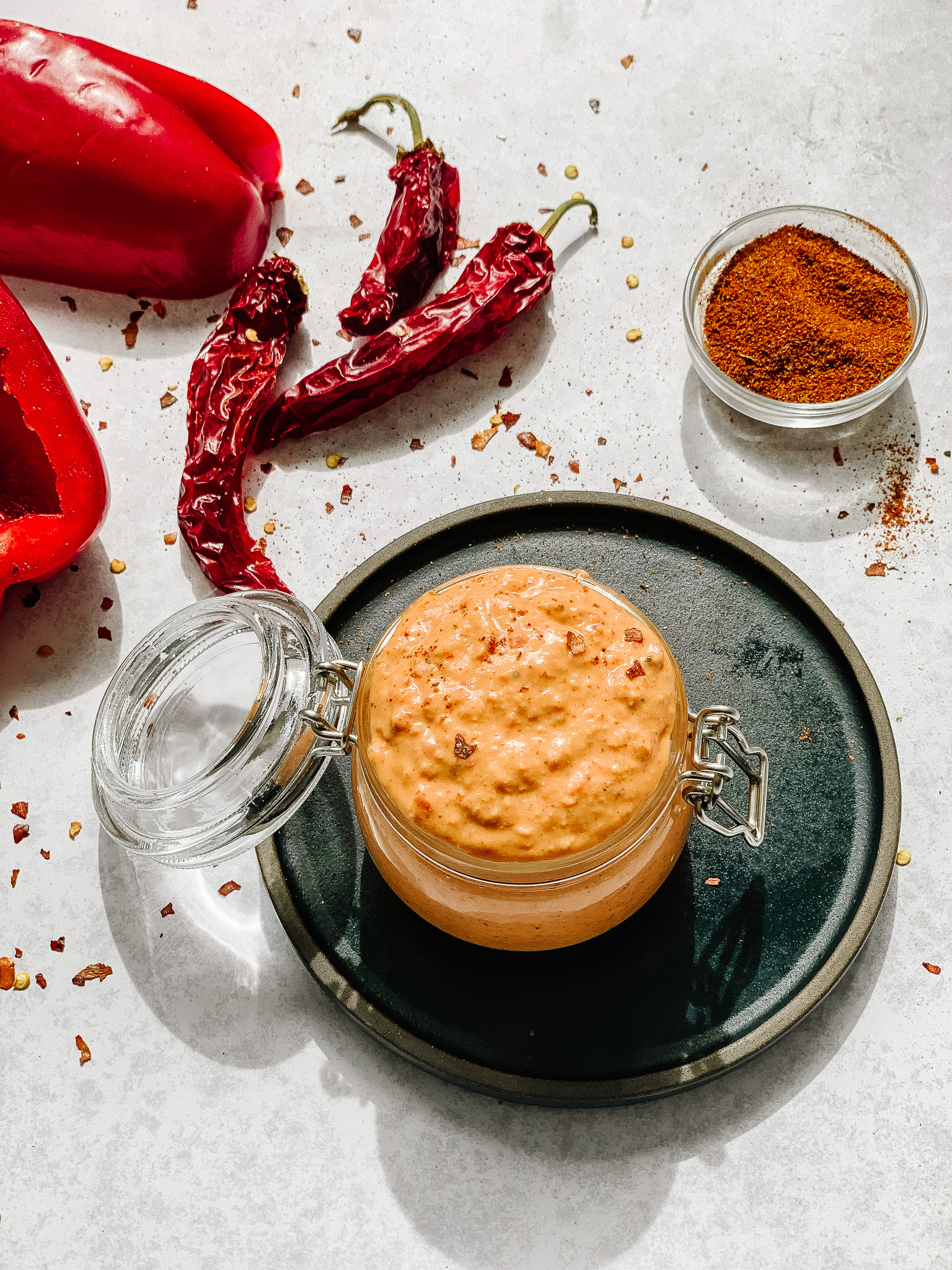 Smoky Red Pepper Drizzle in a jar with paprika and peppers surrounding