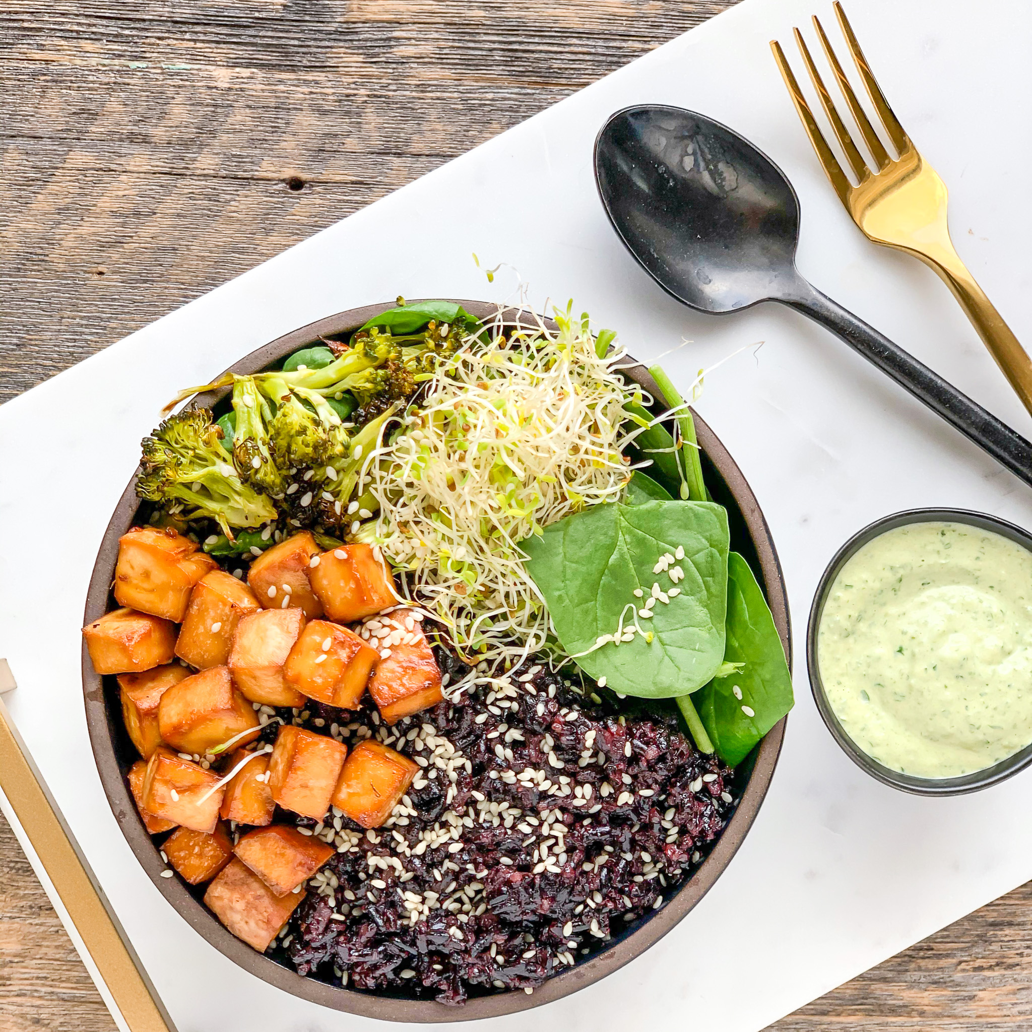 Garlic Tahini Sauce beside a bowl with cabbage, yams, avocados, and other goodness