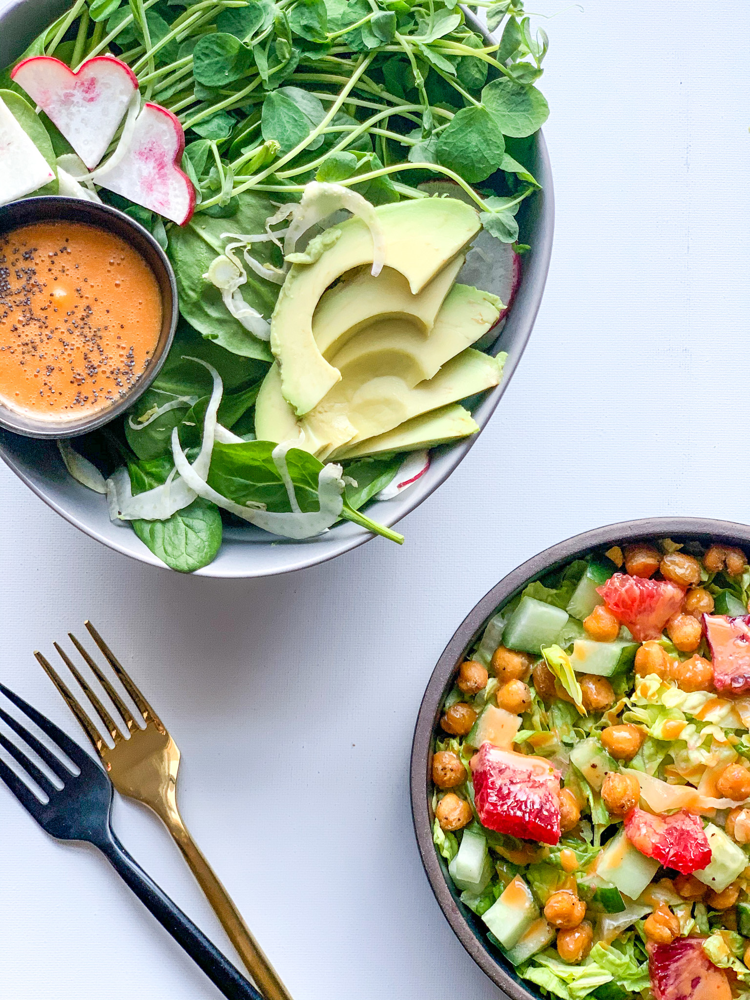 Two bowls and forks, one wit avocado, spinach and sweet and spicy sauce. The other has chic peas and tomato salad